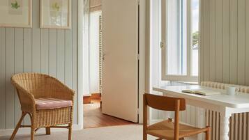 A room with a wicker chair, a white table, and a window with striped curtains.