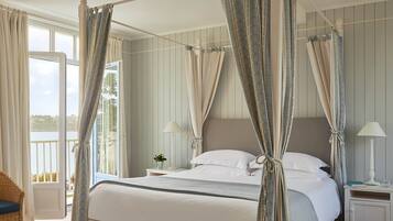 A four-poster bed with curtains, a nightstand with a lamp, and a view of the outdoors.
