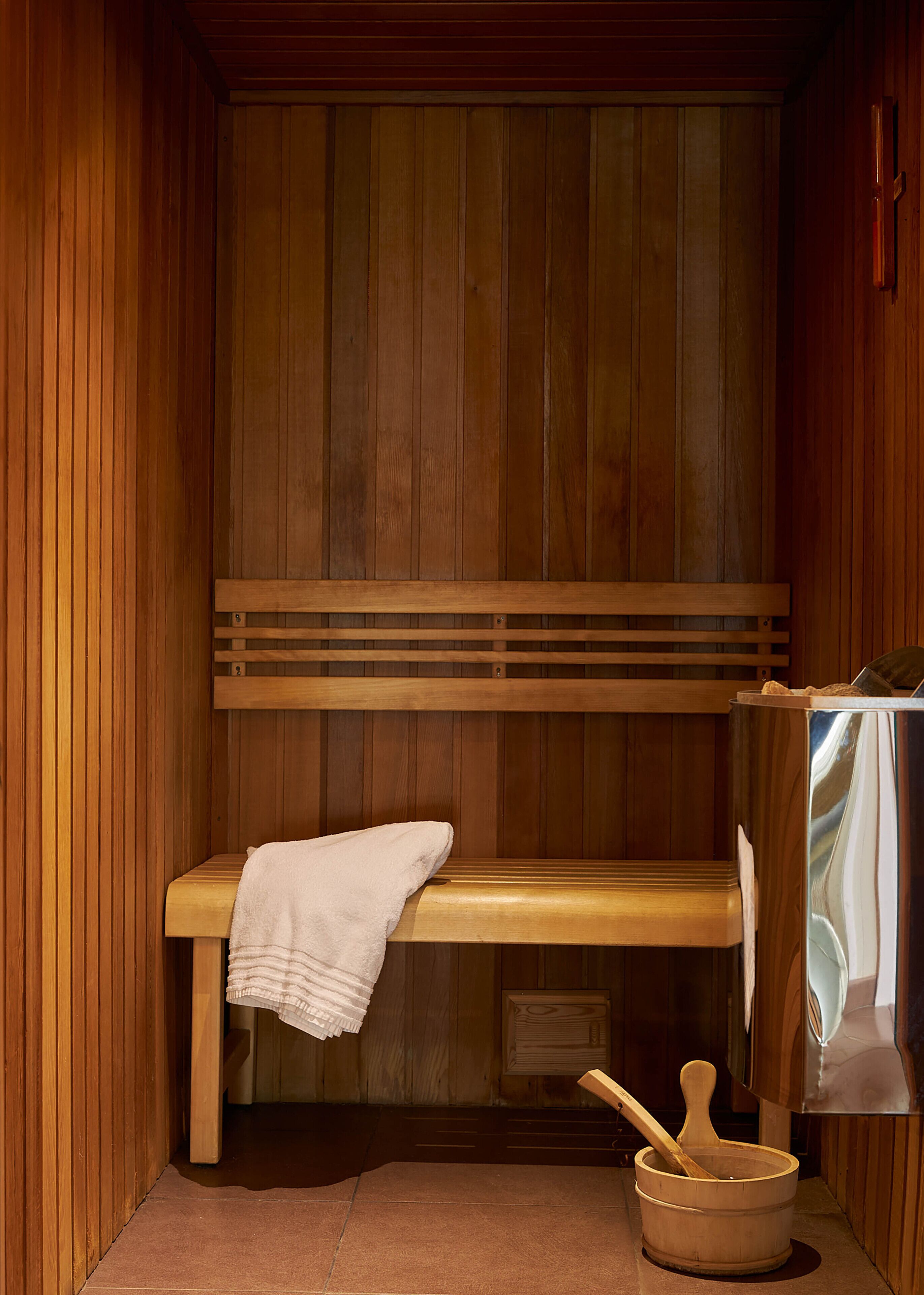 A sauna room with wooden benches, a bench with a towel, and a wooden bucket with a wooden mallet.