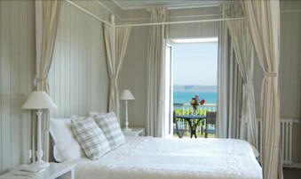 Un dormitorio con una cama, dos mesitas de noche con lámparas y vista al mar por una puerta abierta.