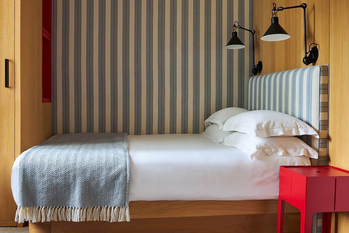 A bedroom with a bed, a red nightstand, and two black desk lamps.