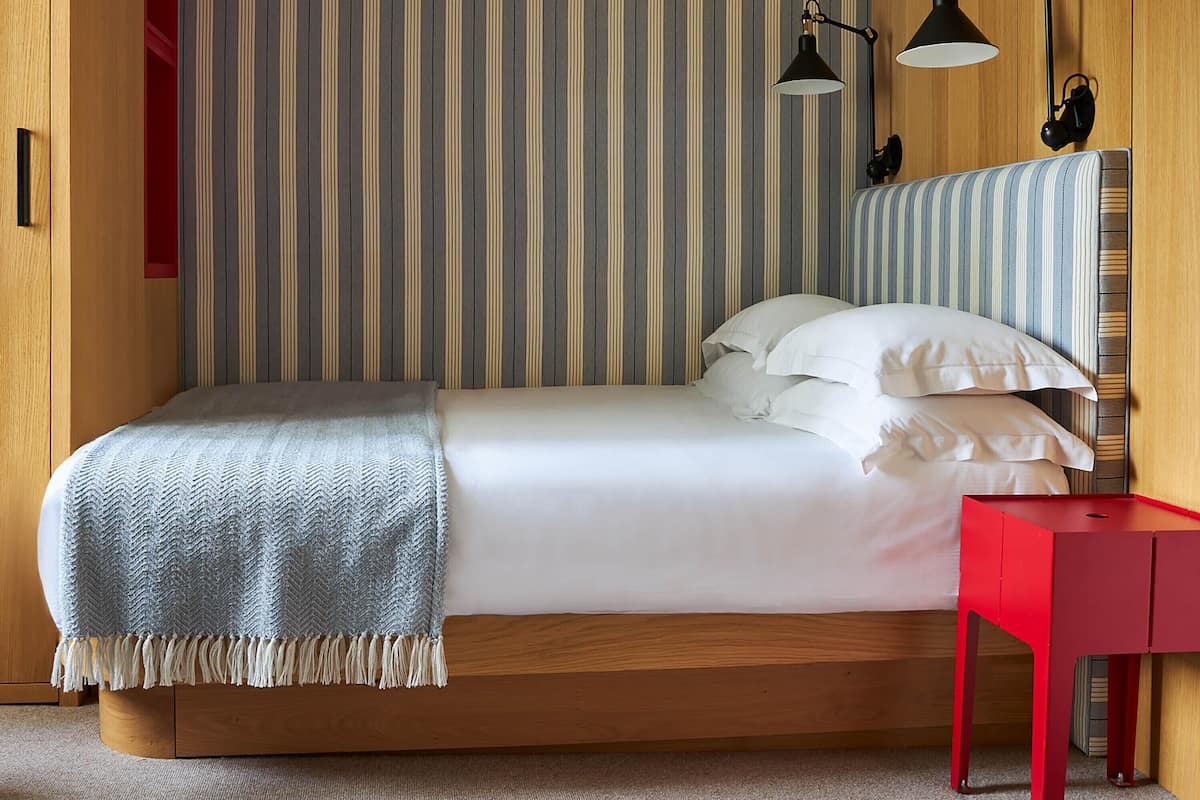 A bedroom with a bed, a red nightstand, and two black desk lamps.
