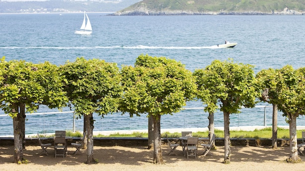 A seaside park with trees, benches, and a view of the sea with boats. - Le Grand Hotel des Bains & Spa - Bretagne (Locquirec)