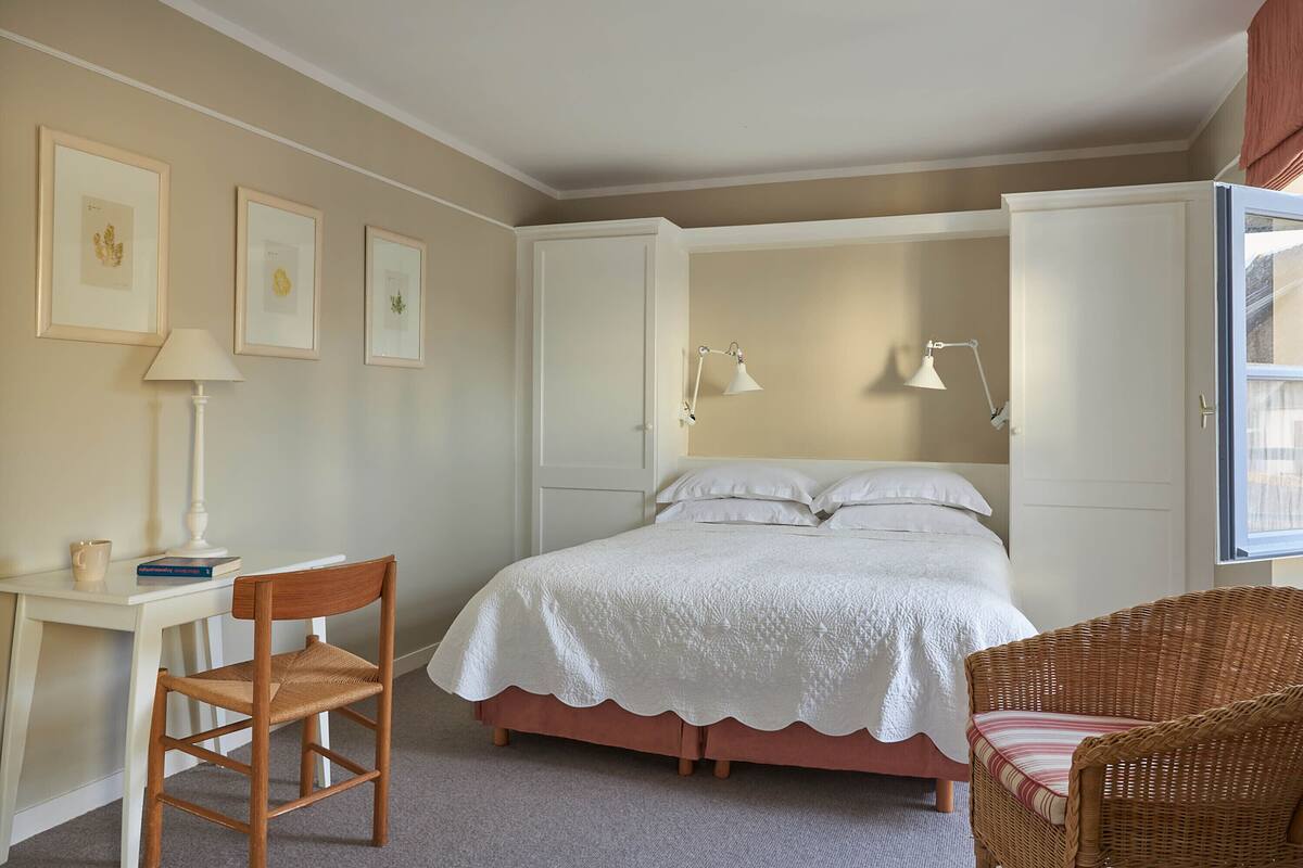 A bedroom with a bed, a chair, a desk, and framed pictures on the wall.