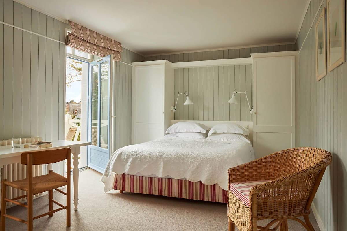 A bedroom with a bed, a desk, a chair, and a wicker chair.