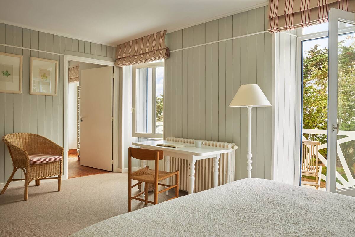 A bedroom with a bed, a desk, a chair, and a window with a view of the outdoors.
