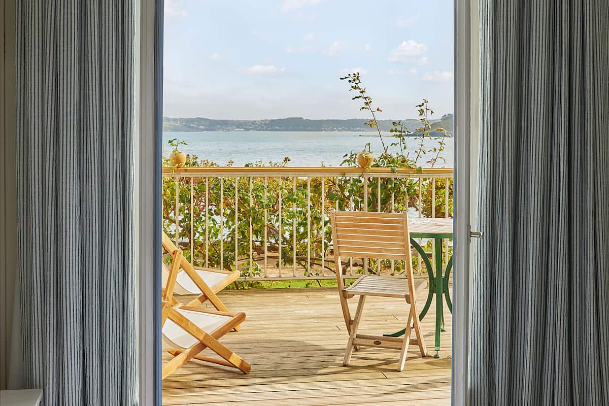 A room with a large window, a wooden deck, and a view of the sea.