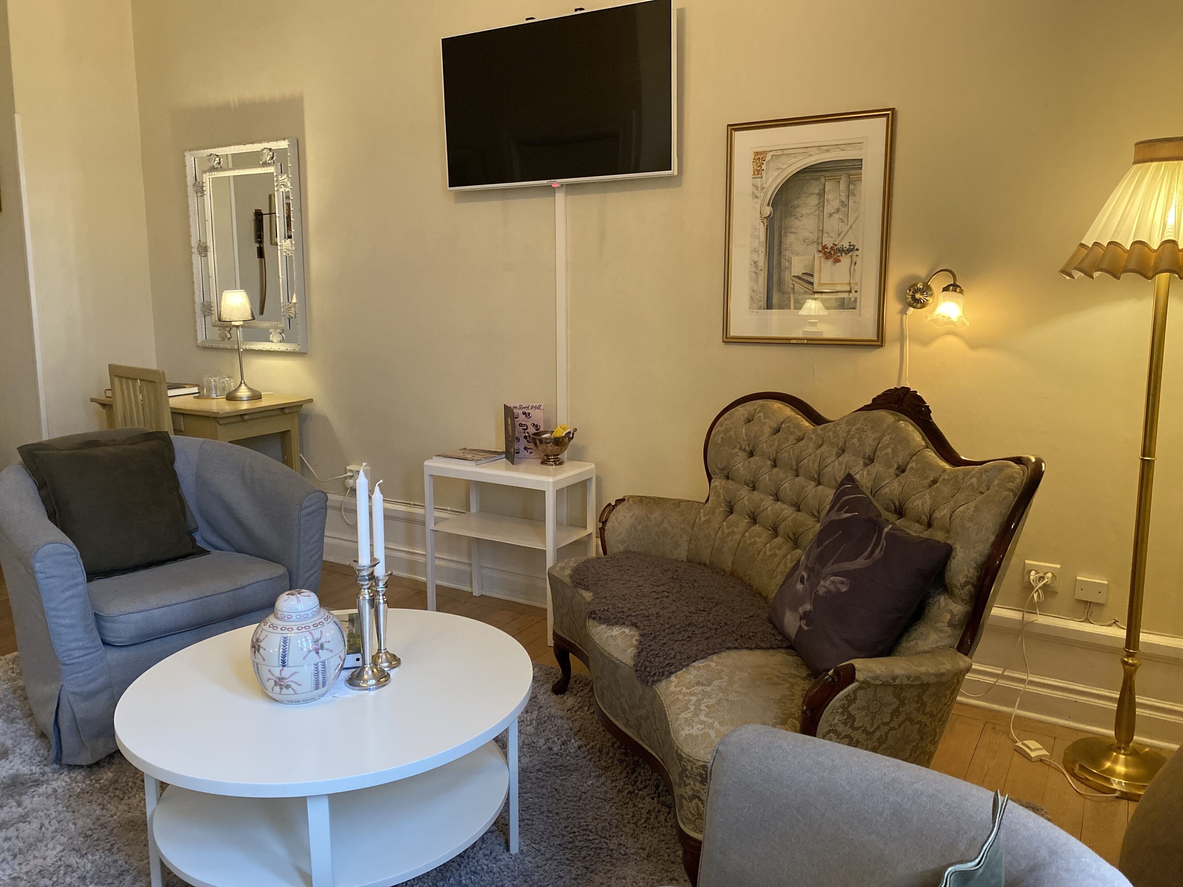 Una sala de estar con un sofá gris, una mesa redonda de café blanca, un sillón capitoné y una lámpara de pie.