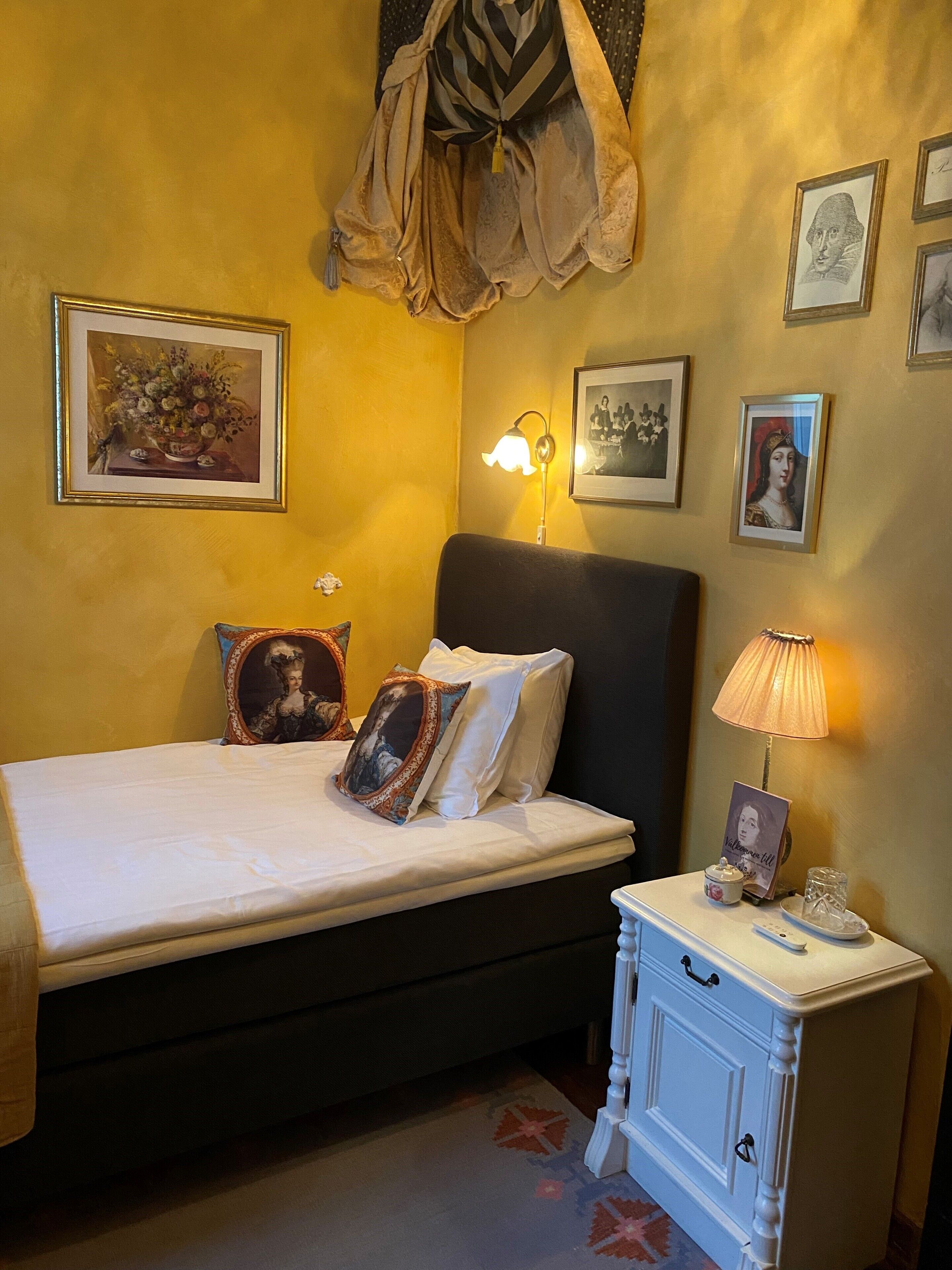 A bedroom with a bed, bedside table, lamp, and framed pictures on the wall.