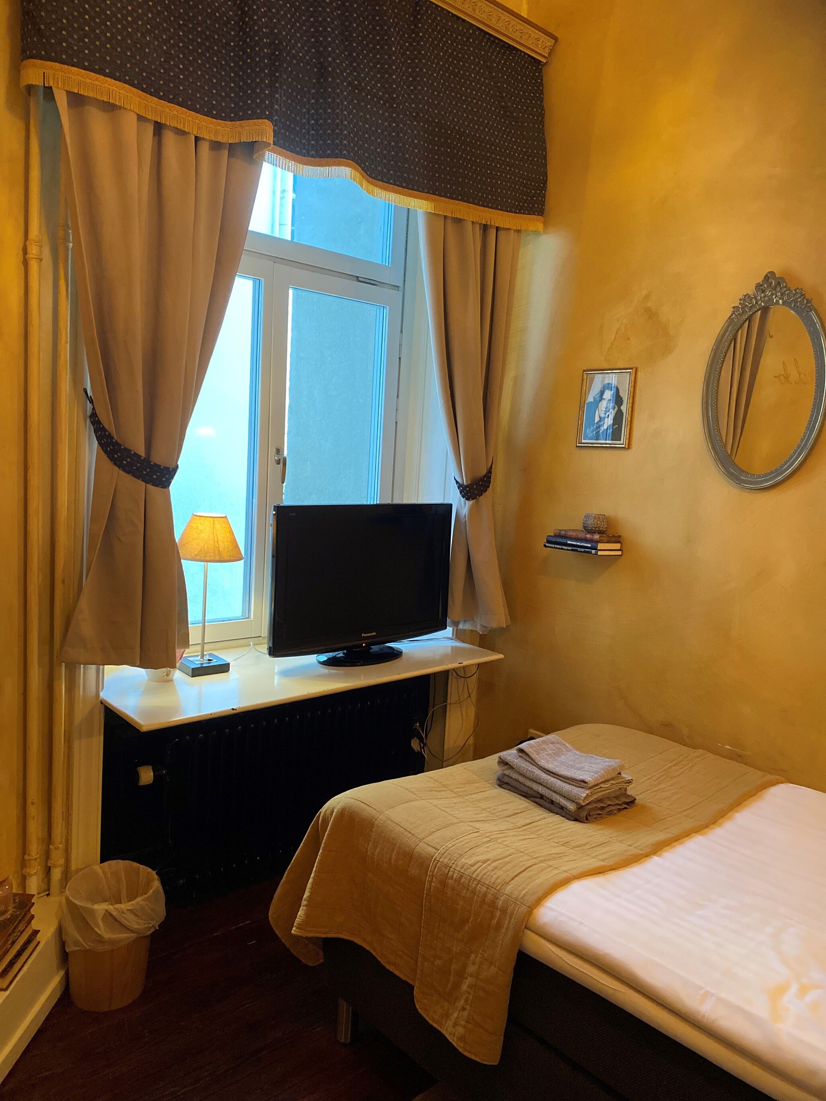 Un cuarto de hotel con una cama, un televisor sobre un escritorio, una lámpara, un espejo y un cuadro en la pared.