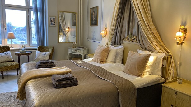 A neatly arranged bedroom with a large bed, a bedside table, a lamp, and a chair. - Strand Hotell (Norrköping)