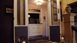 A hotel entrance with a sign reading "Strand Hotel," a white door, a chandelier, and a small table with a vase of flowers. - Strand Hotell (Norrköping)