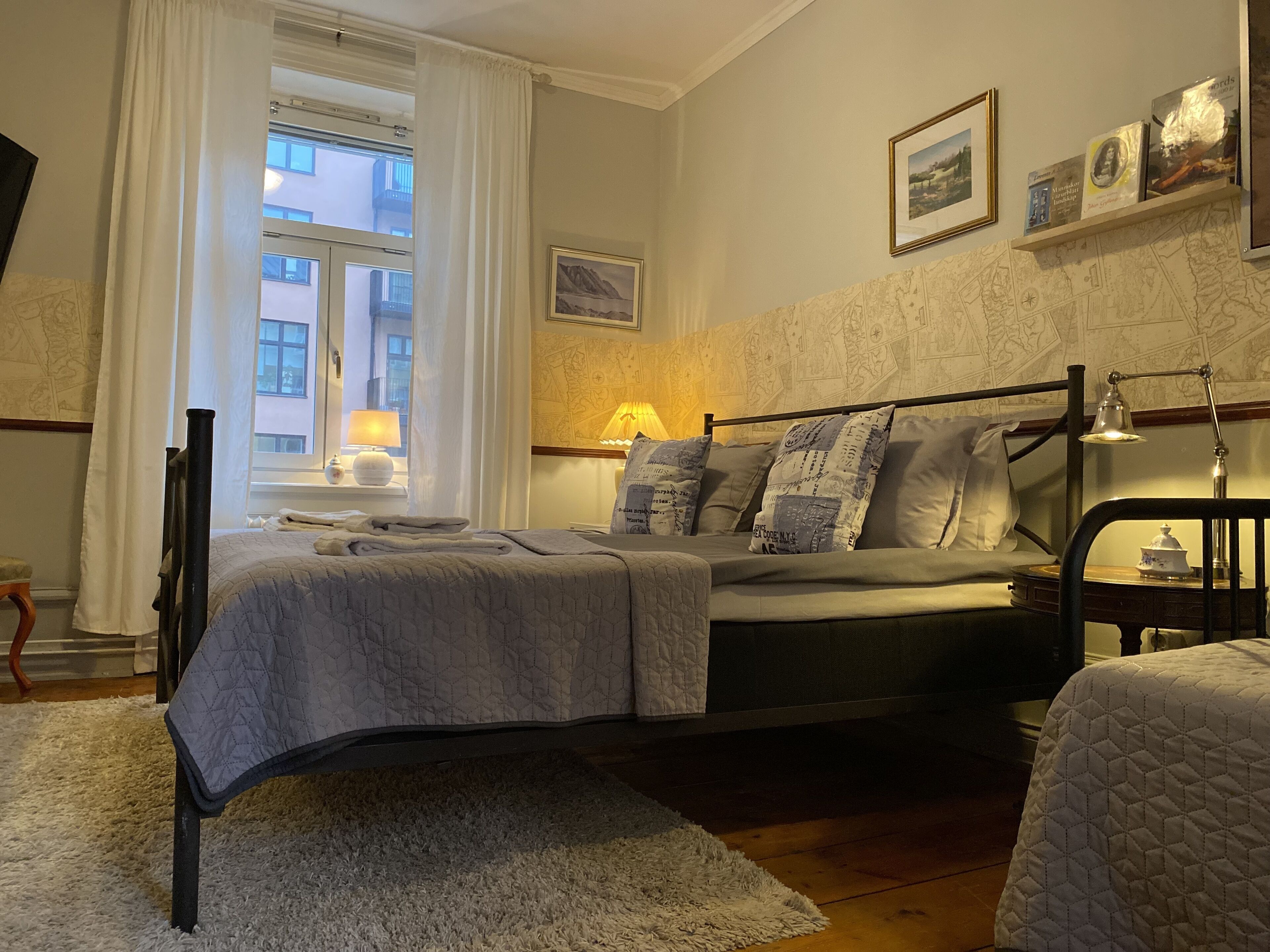 A neatly arranged bedroom with a bed, a bedside table, a lamp, and a window with curtains.