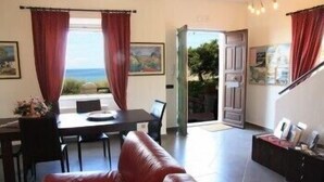 Ein Zimmer mit Esstisch, Stühlen, einem roten Sofa und Blick ins Freie.
