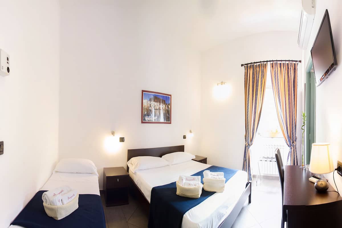 Une chambre d’hôtel avec deux lits simples, un bureau avec une lampe, une chaise et une fenêtre avec des rideaux.