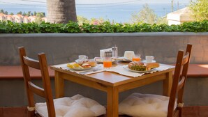 Ein Holztisch mit Frühstücksangebot, zwei Stühle und Blick aufs Meer.