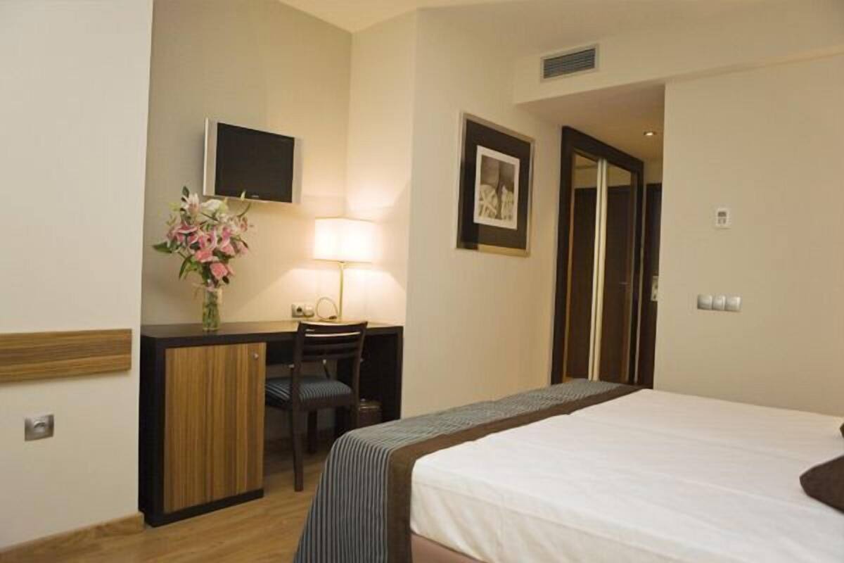 Ein Hotelzimmer mit Bett, Schreibtisch mit Stuhl, einem an der Wand befestigten Fernseher und einem gerahmten Bild.