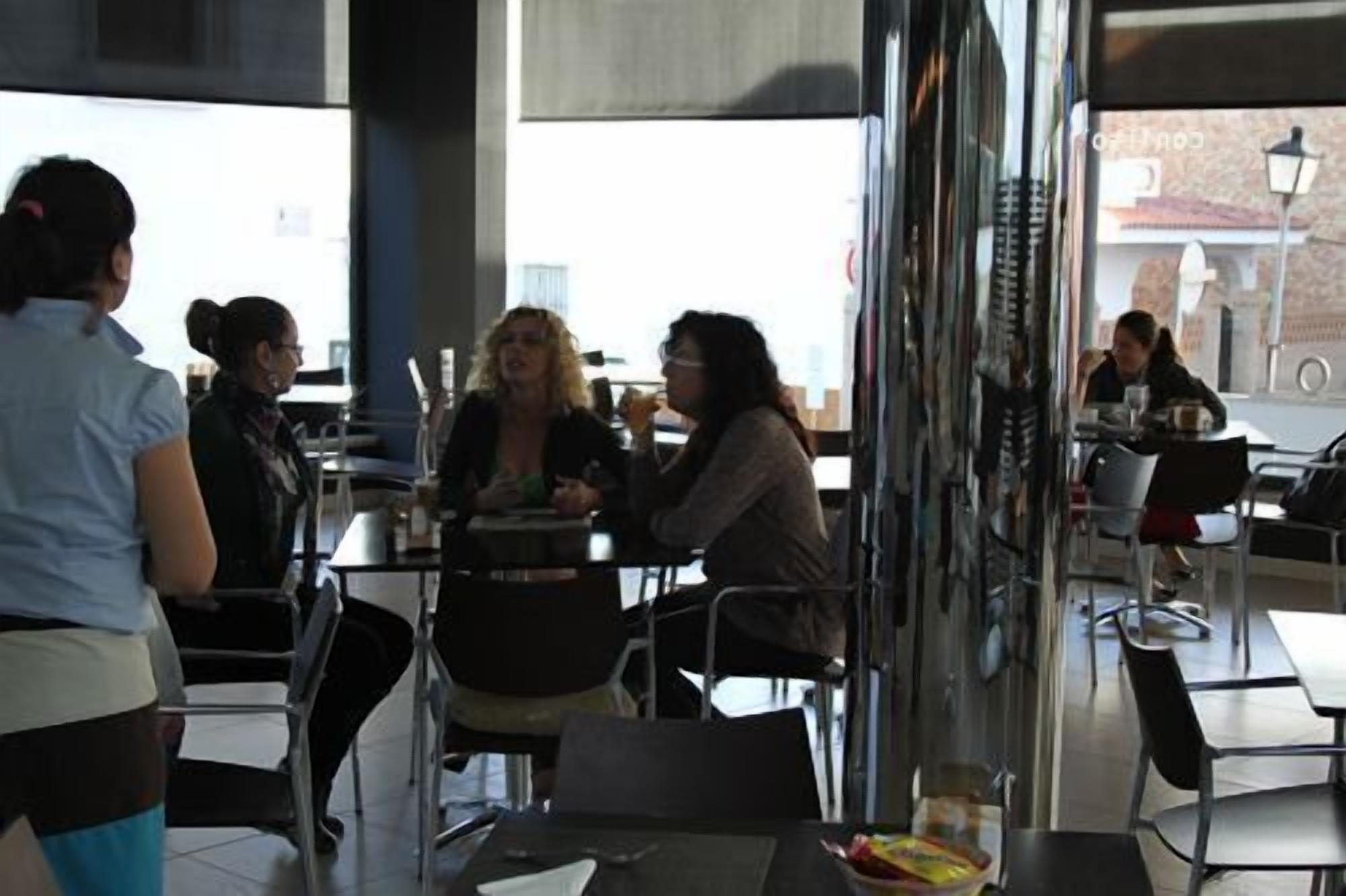 An outdoor cafe with tables and chairs, a glass partition, and a view of the street.