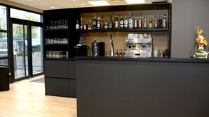 A modern bar area with shelves of liquor bottles, a coffee machine, and a decorative flower arrangement.