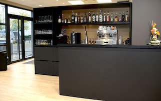 Uma área de bar moderna com prateleiras cheias de garrafas de bebidas, uma máquina de café e um arranjo floral decorativo.