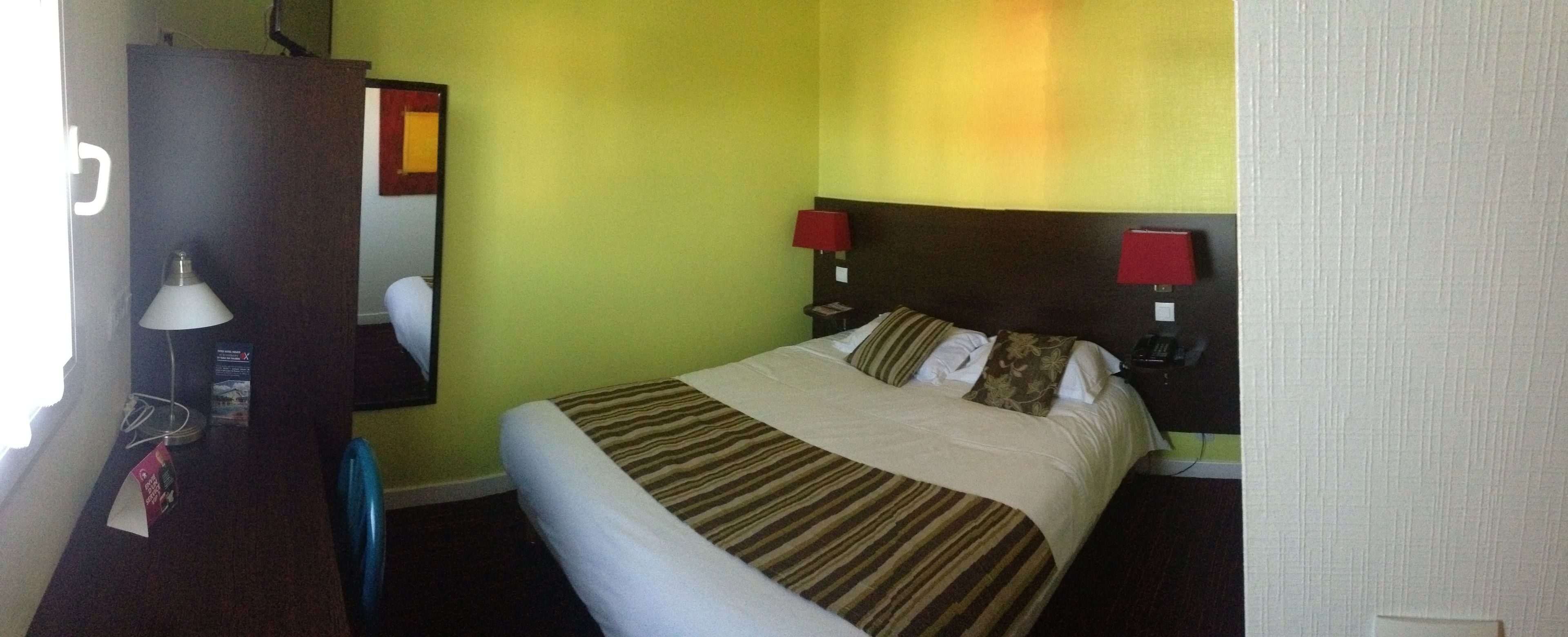 Una habitación de hotel con cama, dos lámparas de noche, una mesita de noche, un espejo y un armario.