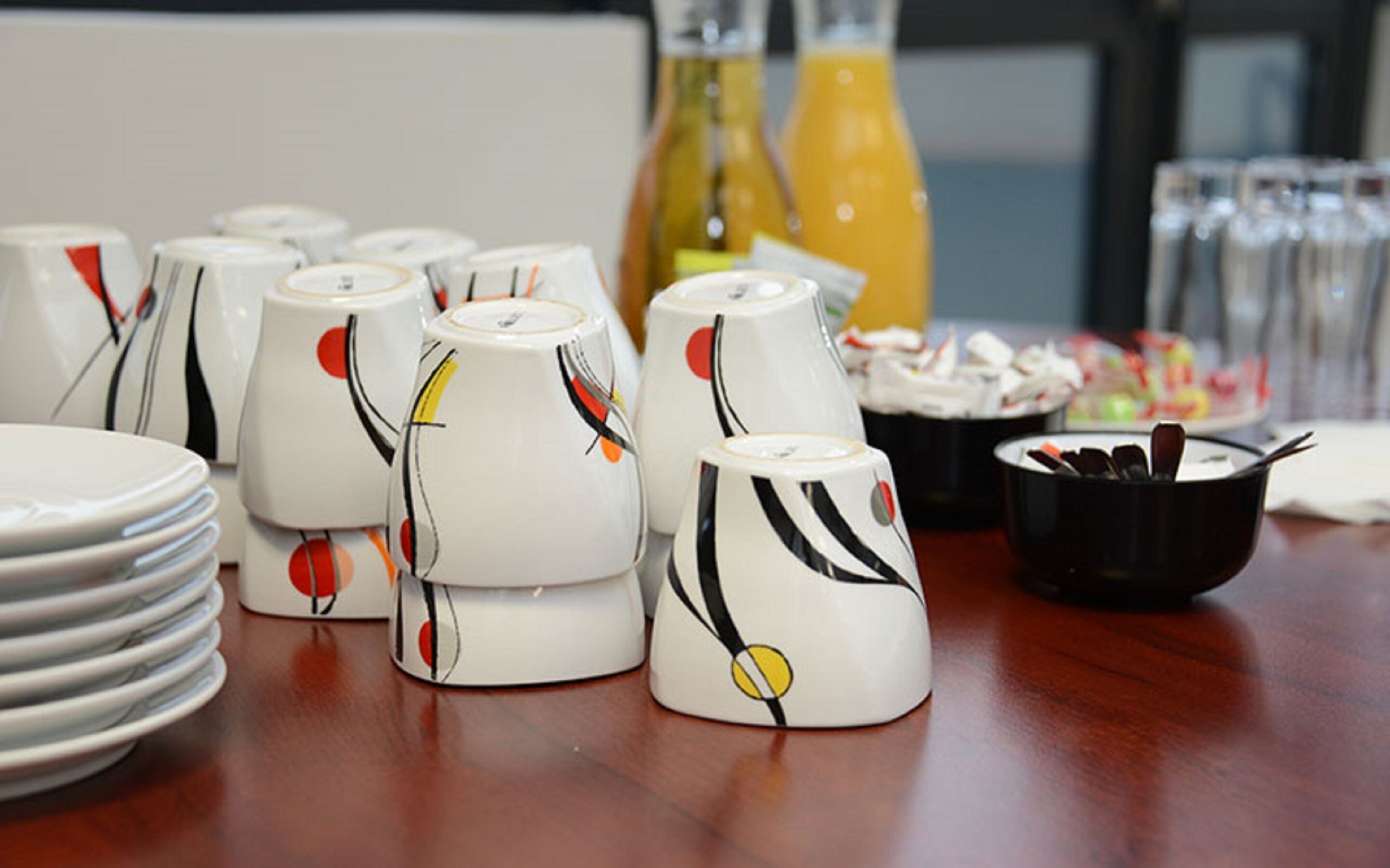 Uma mesa com chávenas de cerâmica branca com designs abstratos, pratos e uma tigela preta com utensílios.