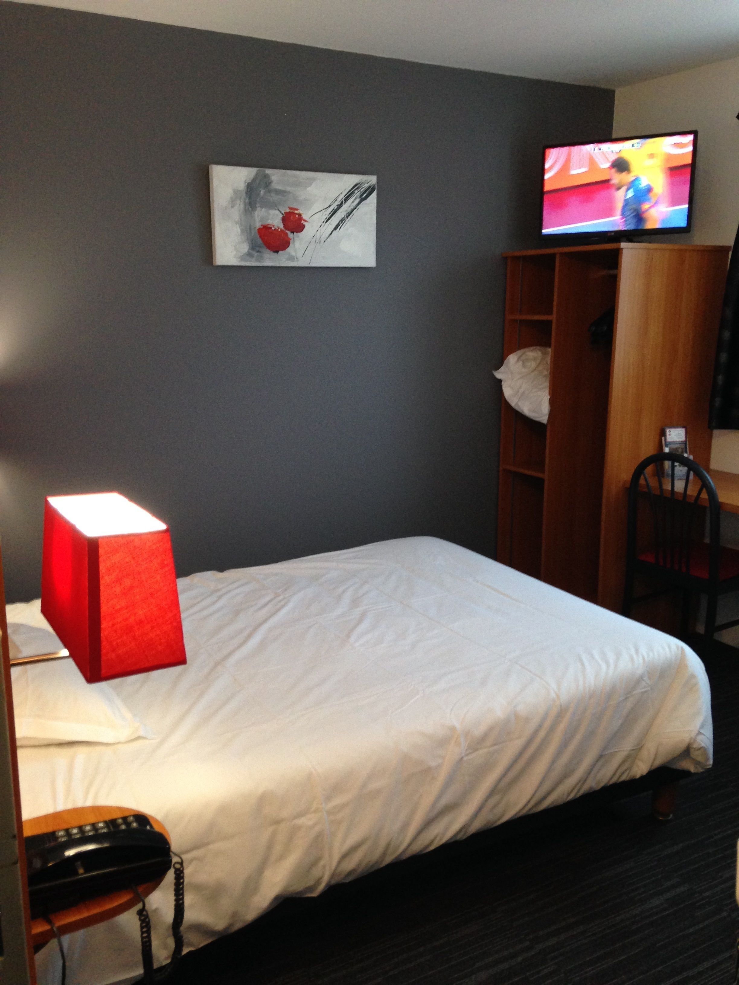A hotel room with a bed, a TV on the wall, a painting, and a wooden cabinet.