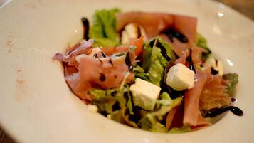 A plate with a salad consisting of greens, tomatoes, cheese, and prosciutto.