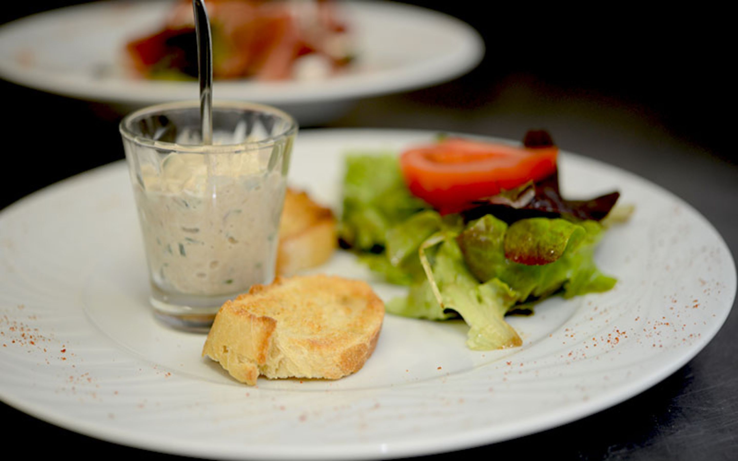 Ein Teller mit Suppe, einem Brotscheibe und einem Salat mit einer Tomate.