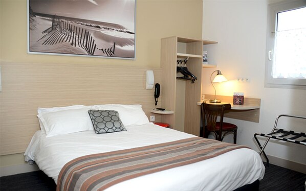 Habitación de hotel con cama, escritorio con lámpara, silla, teléfono y ventana.