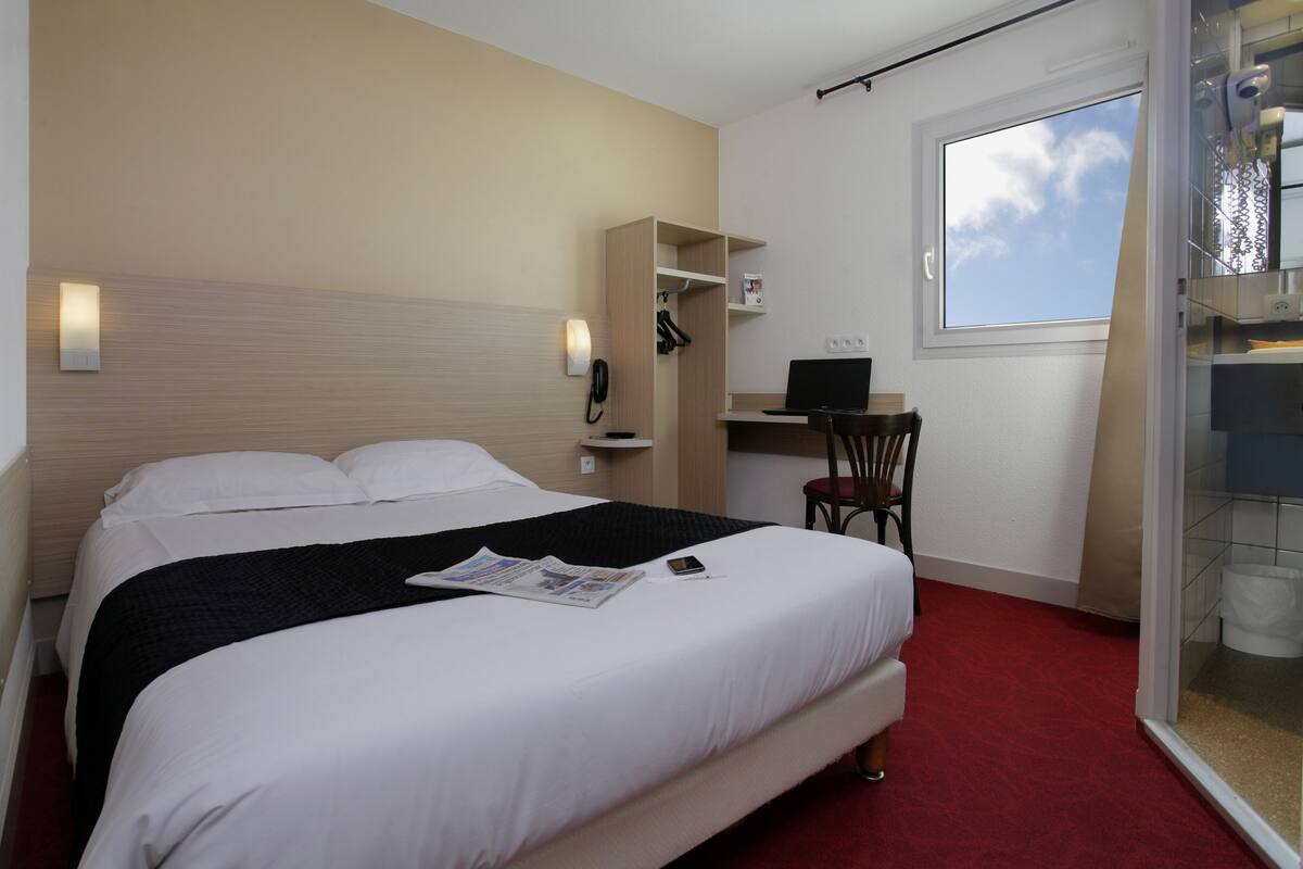 Habitación de hotel con cama, escritorio, silla, teléfono y ventana.