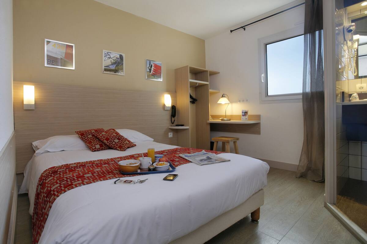Una habitación de hotel con cama, bandeja de desayuno, mesita de noche y una ventana con cortinas.