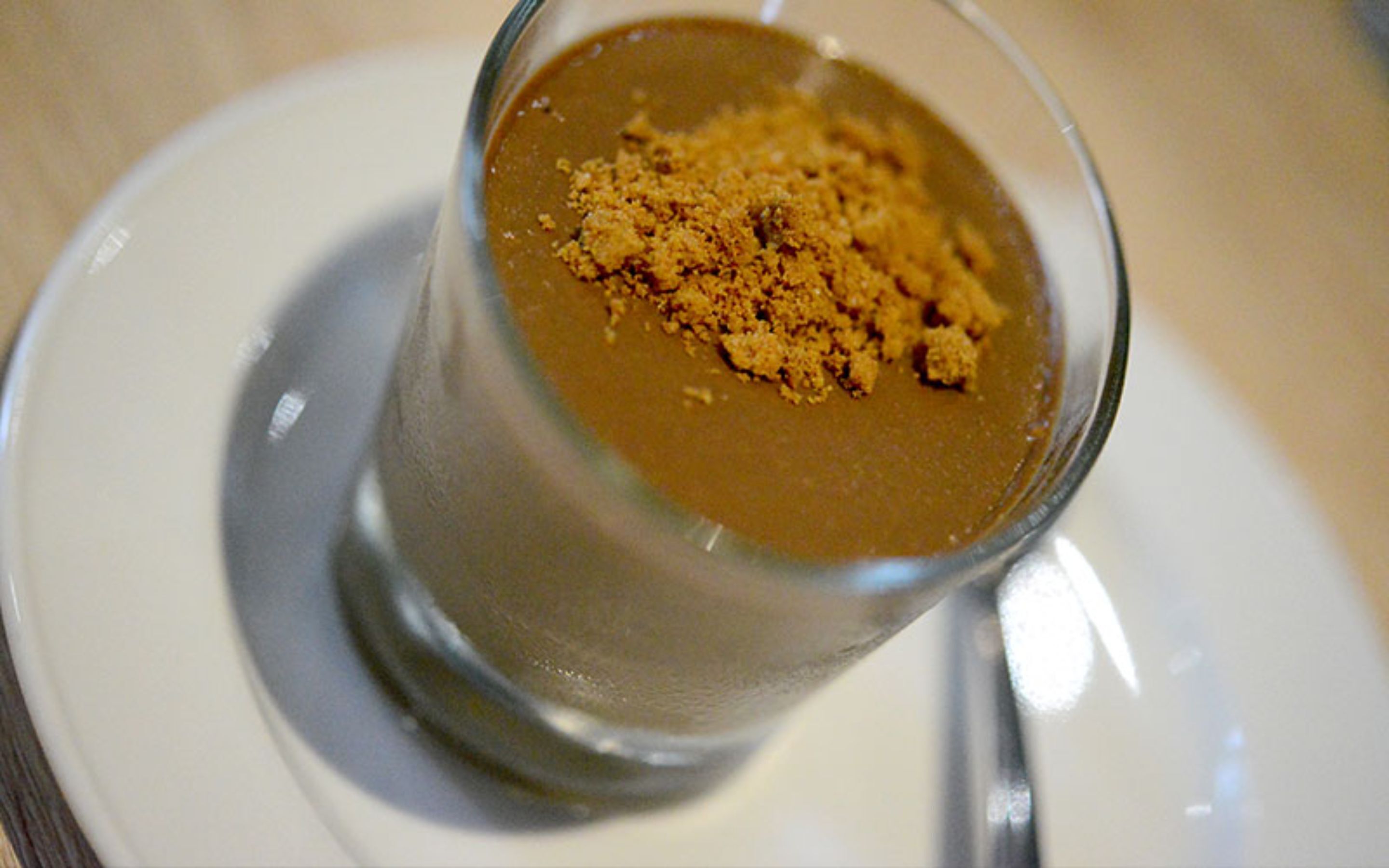 A dessert in a clear glass with a crumb topping, served on a white plate.