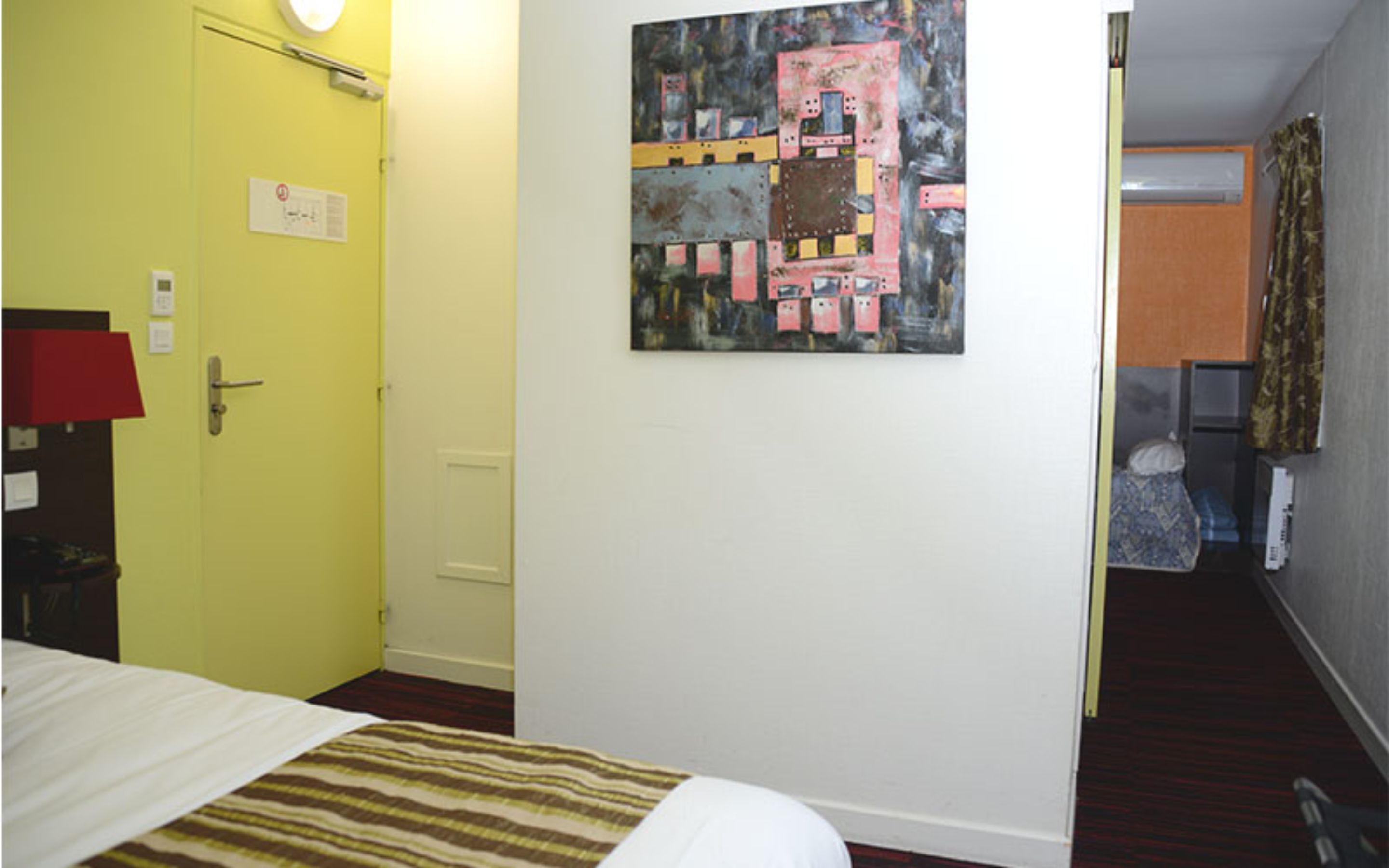 Quarto de hotel com cama, um quadro na parede e porta para o corredor.
