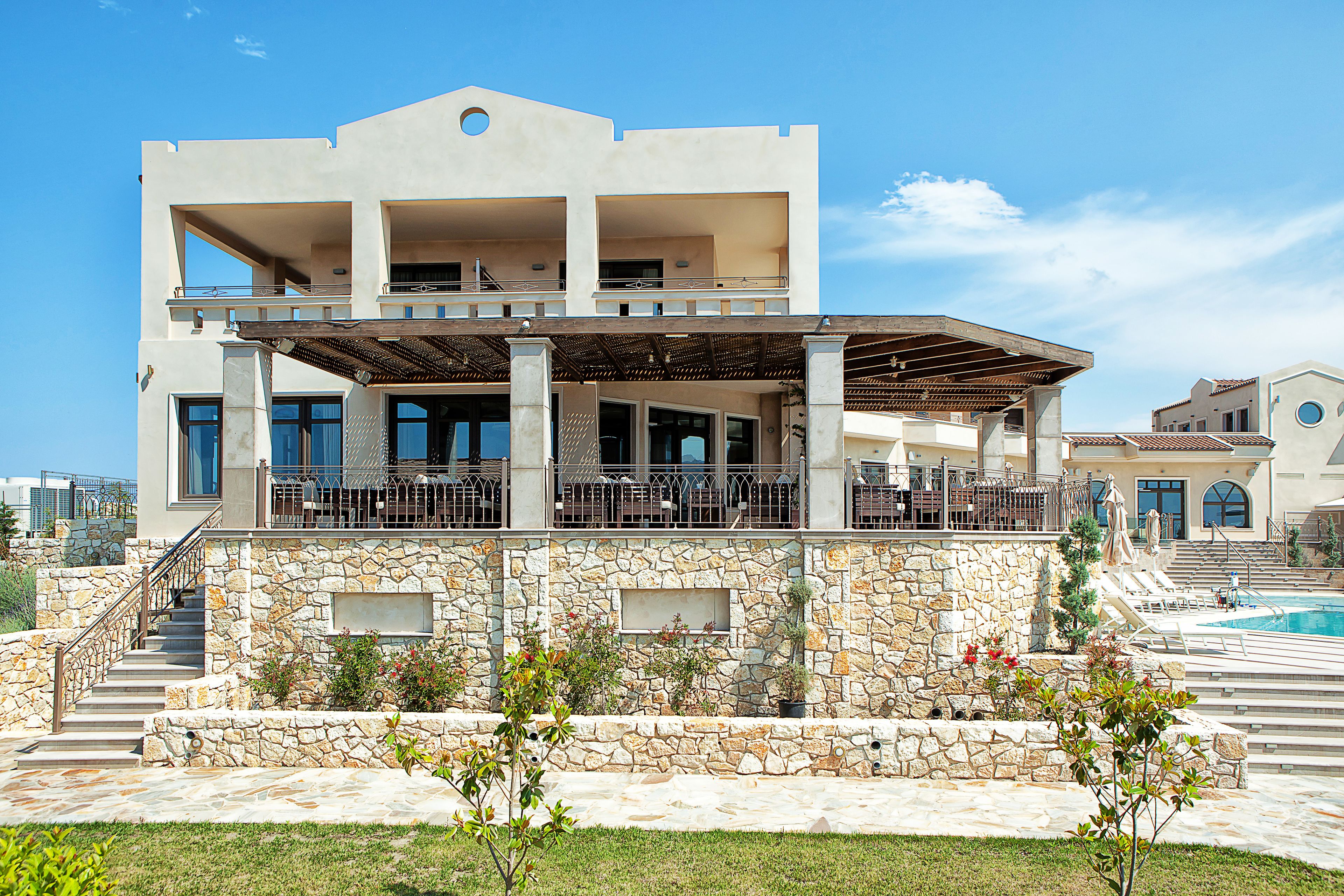 A two-story building with a stone facade, outdoor seating area, and a pool.