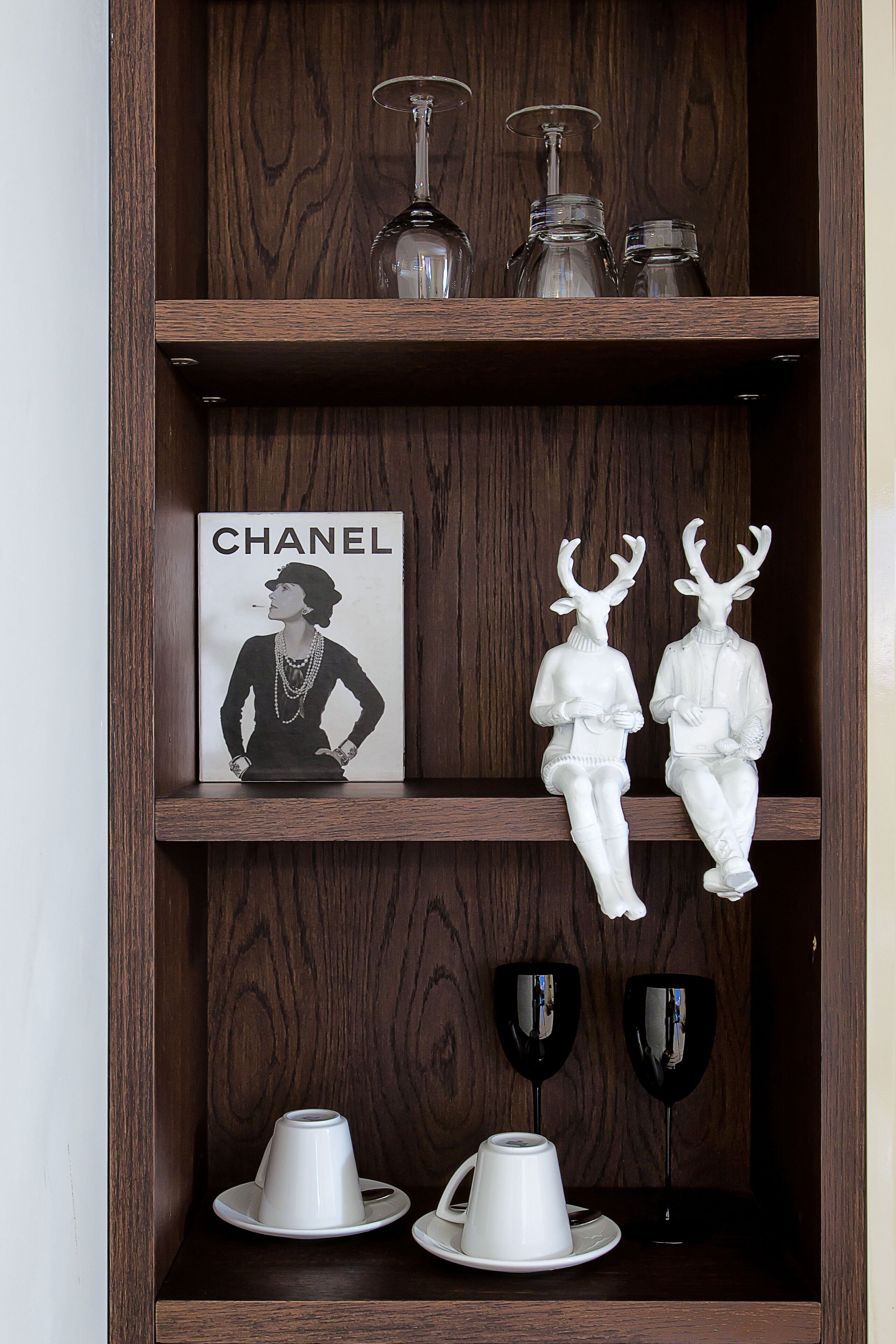 A wooden shelf with a Chanel poster, two reindeer figurines, and wine glasses.