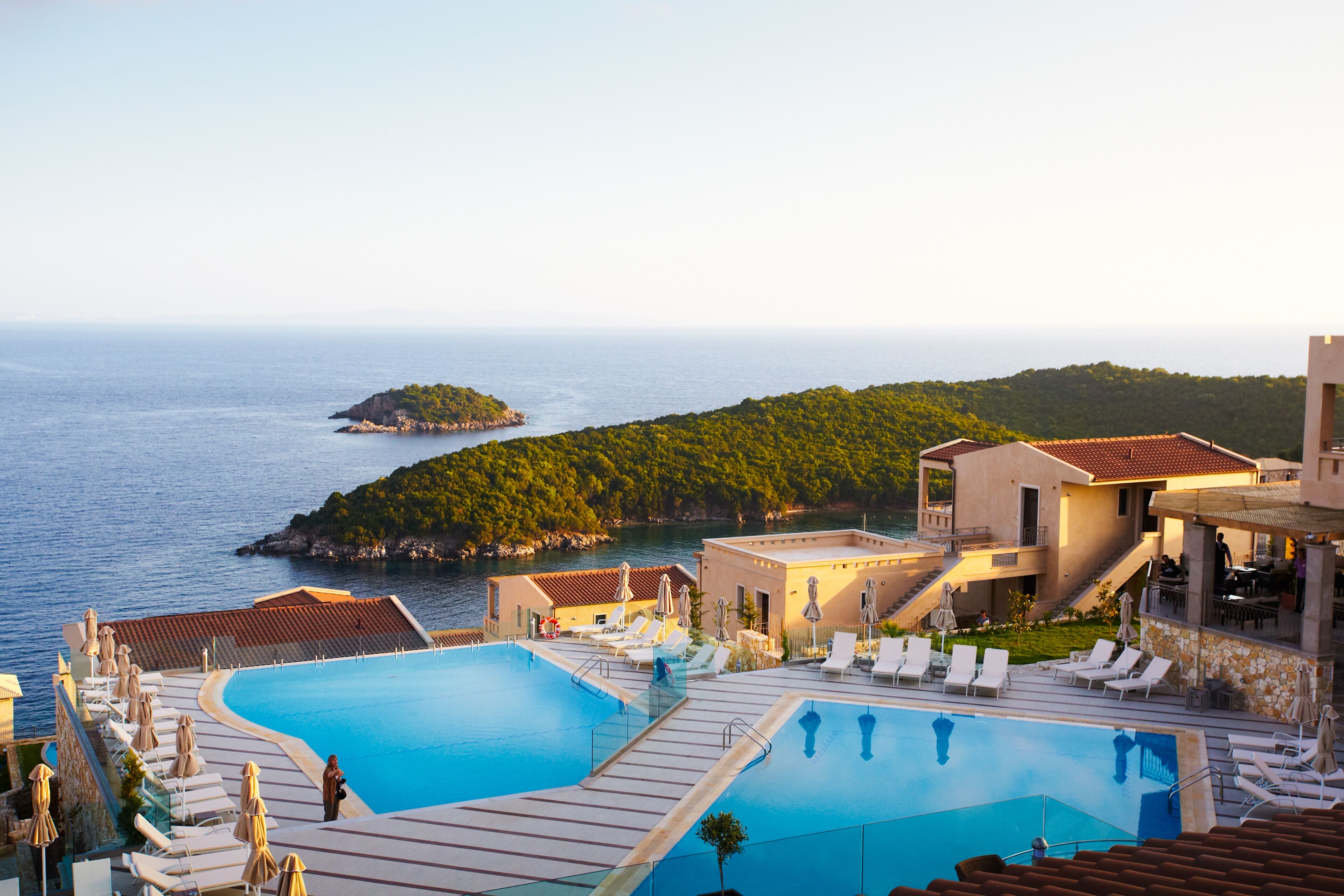 A resort with a large swimming pool, lounge chairs, and a view of the sea and a small island.