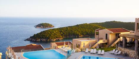 A resort with a large swimming pool, lounge chairs, and a view of the sea and a small island.