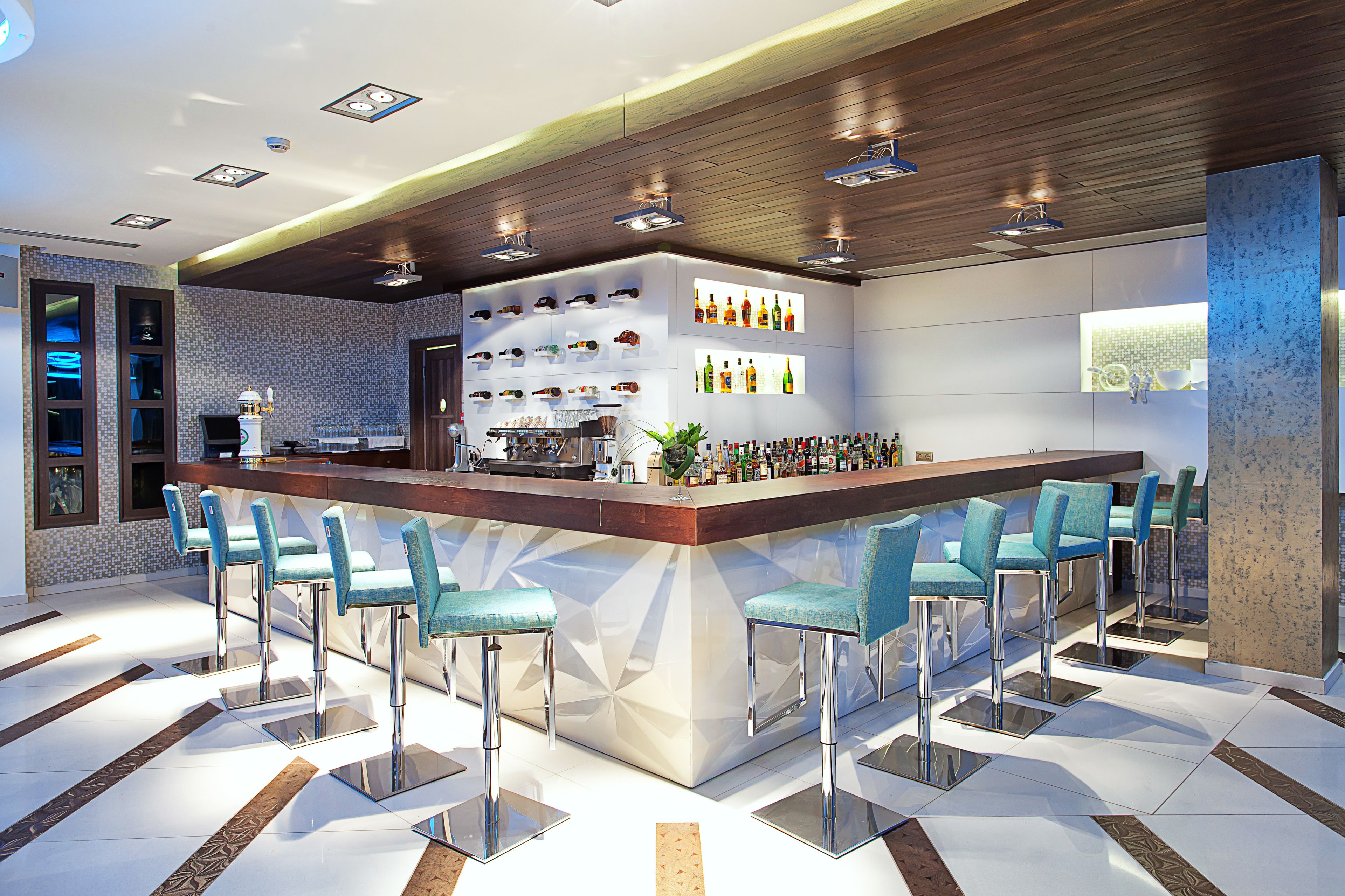 Zona de bar moderna con una barra central, taburetes y una variedad de botellas.