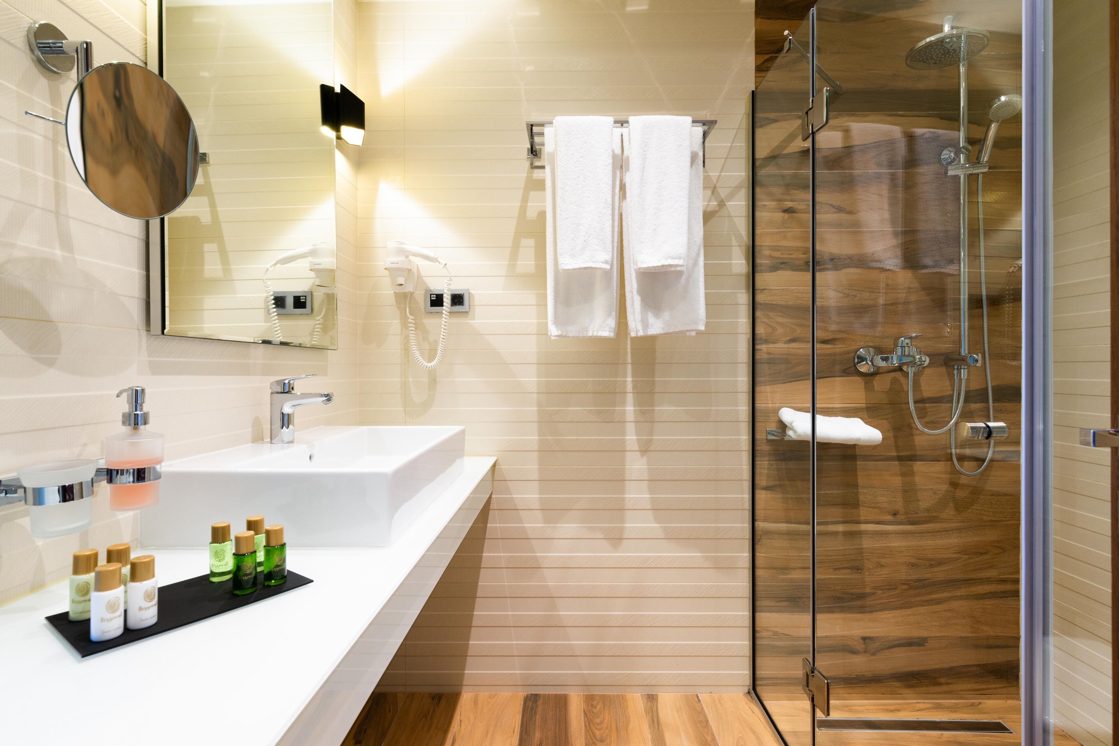 Un baño moderno con un espejo grande, un lavamanos y una ducha con mampara de vidrio.