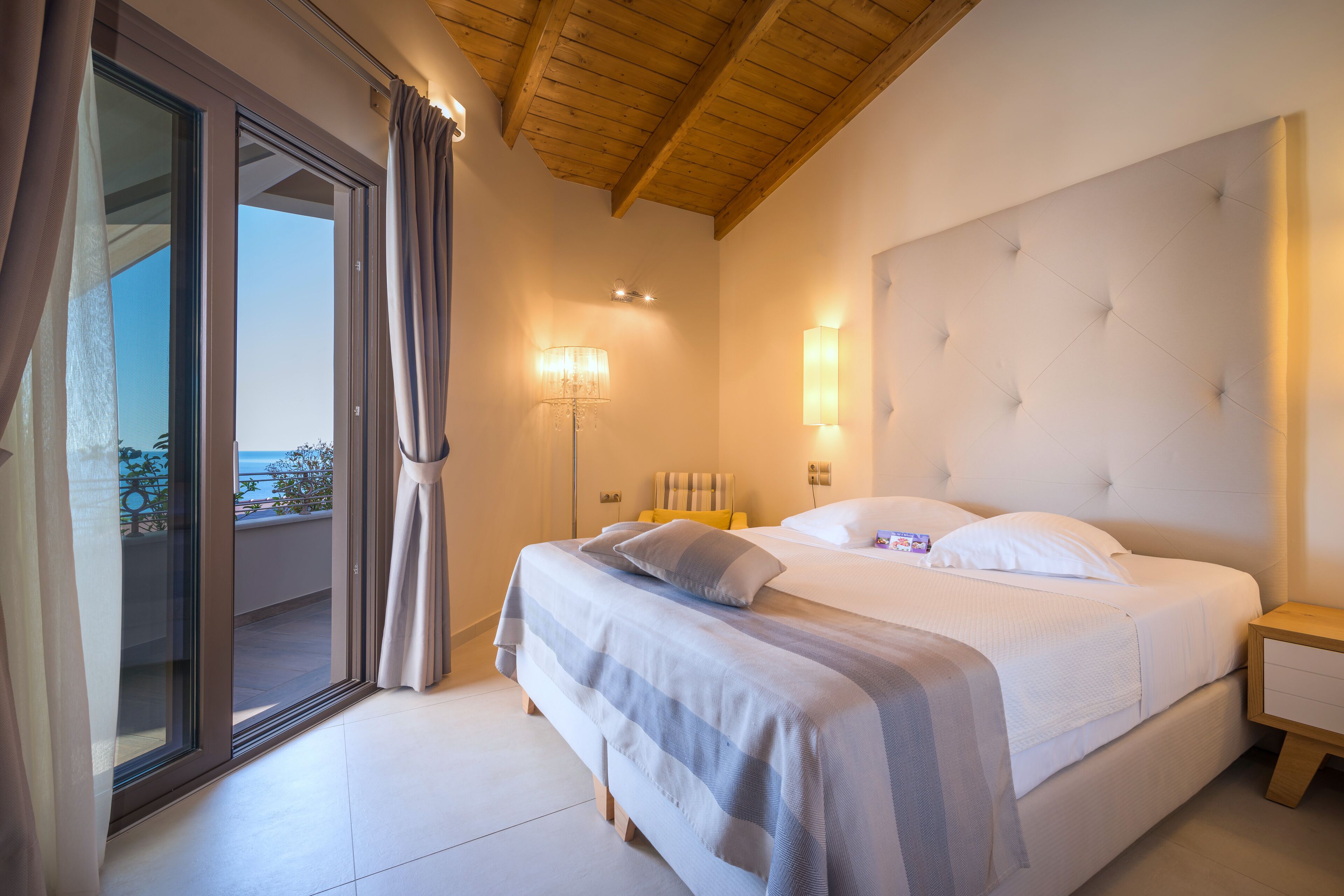 Un dormitorio con una cama grande, una puerta corrediza al balcón, una mesita de noche y una lámpara fijada a la pared.