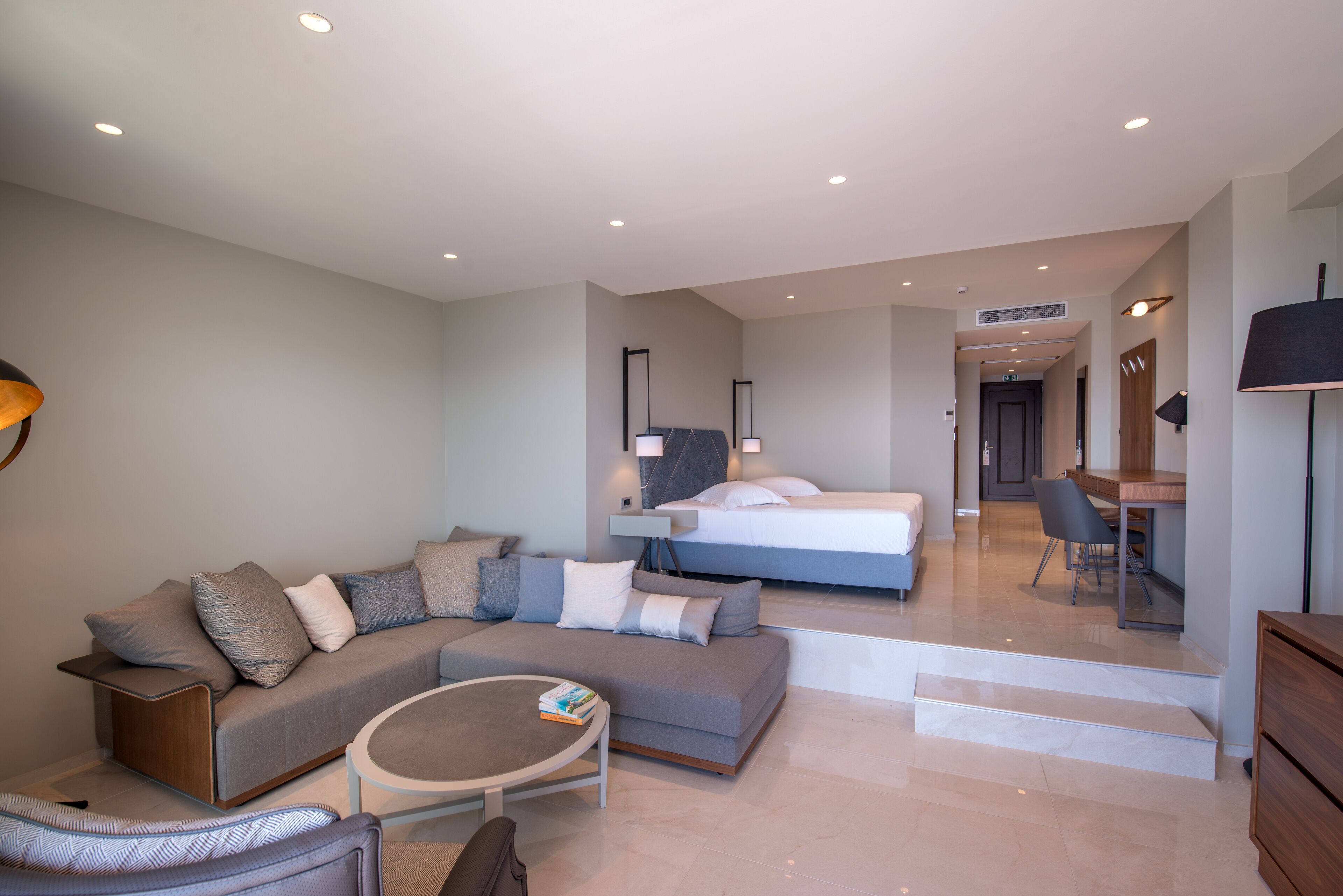 Une chambre d’hôtel moderne équipée d’un canapé, d’une table basse ronde, d’un lit, d’un bureau et d’une chaise.