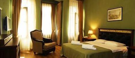 A hotel room with a bed, a chair, a desk, and a lamp.