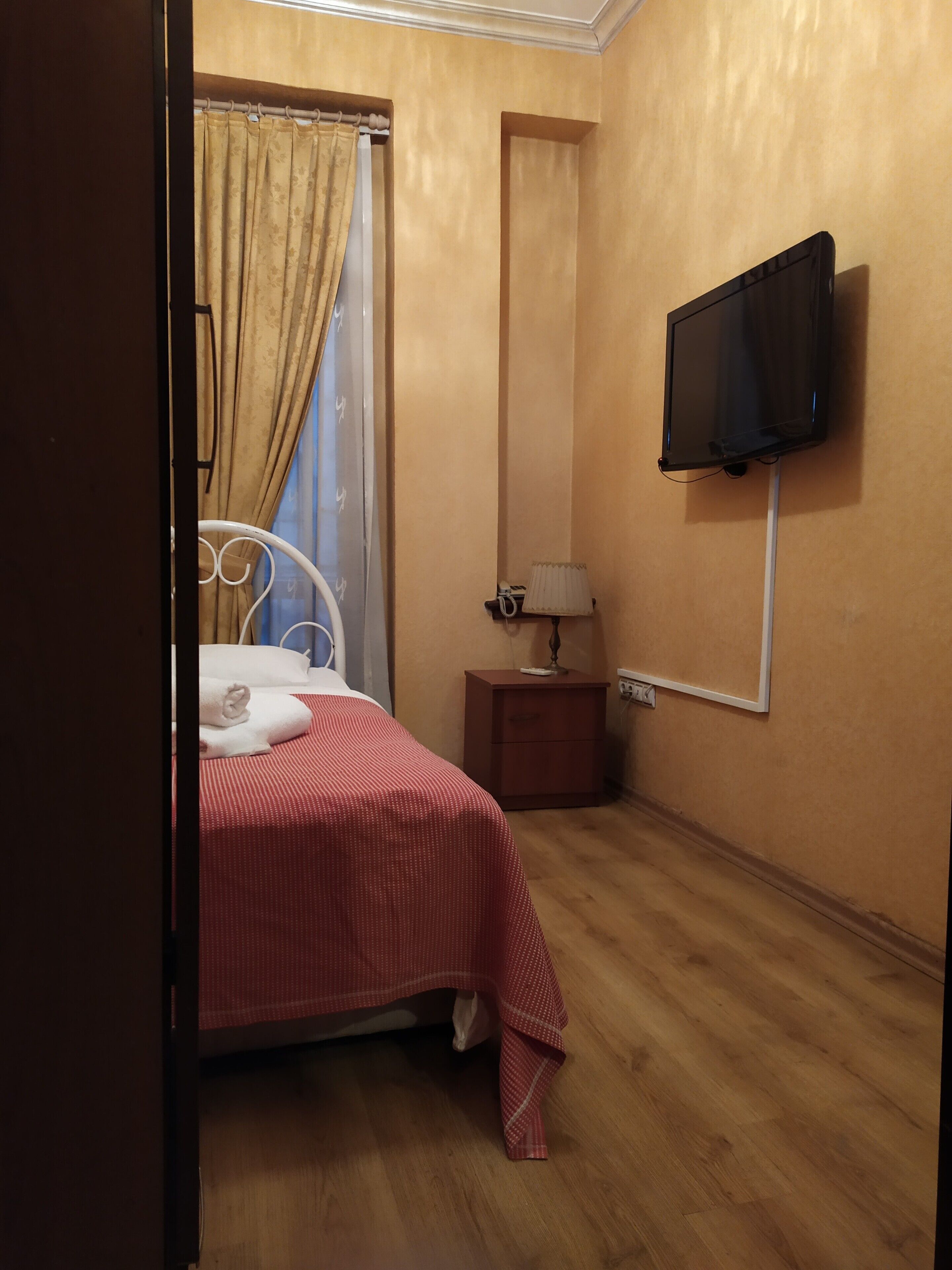 Een hotelkamer met een bed, nachtkastje, een aan de muur bevestigde televisie en een raam met gordijnen.