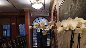 Un pasillo con techo decorativo, alfombra estampada y orquídeas blancas.