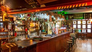 Un bar con suelos de madera, una barra con diversas botellas y taburetes.