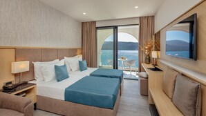 A hotel room with a bed, bedside tables, a TV, and a balcony with a view of the sea. - Hotel Perla (Herceg Novi)
