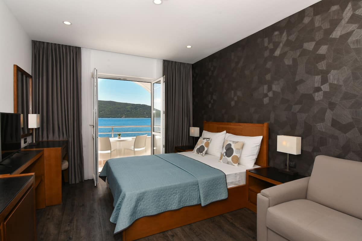 A hotel room with a bed, a desk, a chair, and a view of the sea.