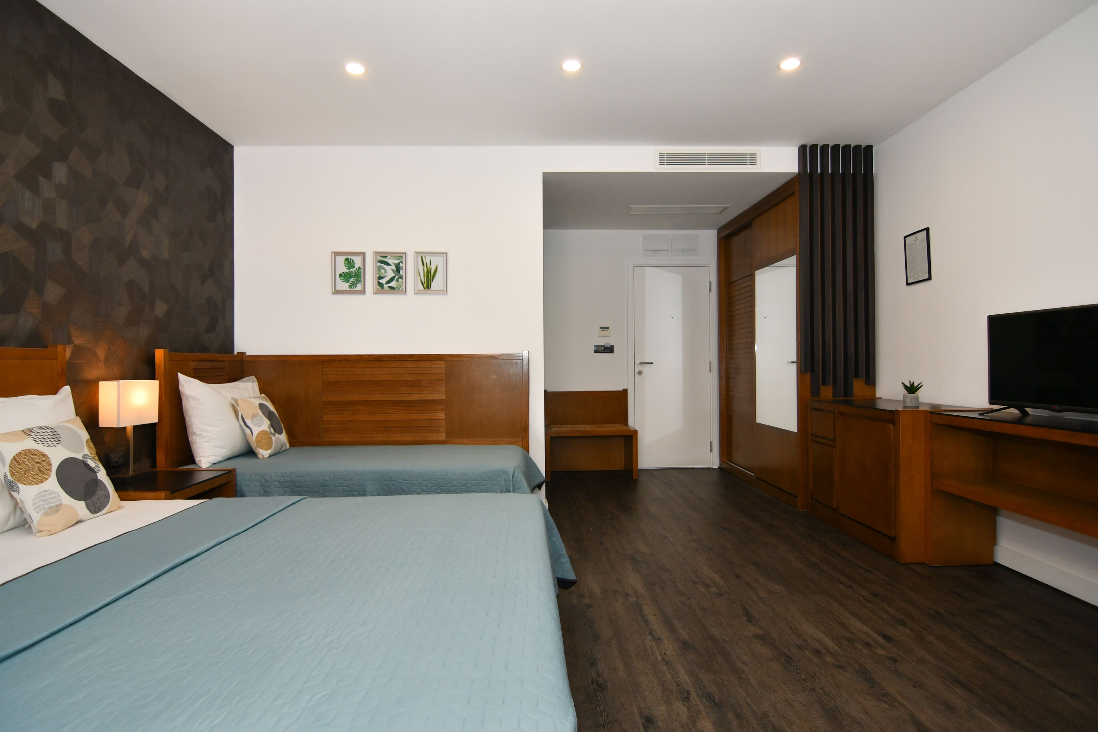 A hotel room with two beds, wooden headboards, a TV, and a small plant.
