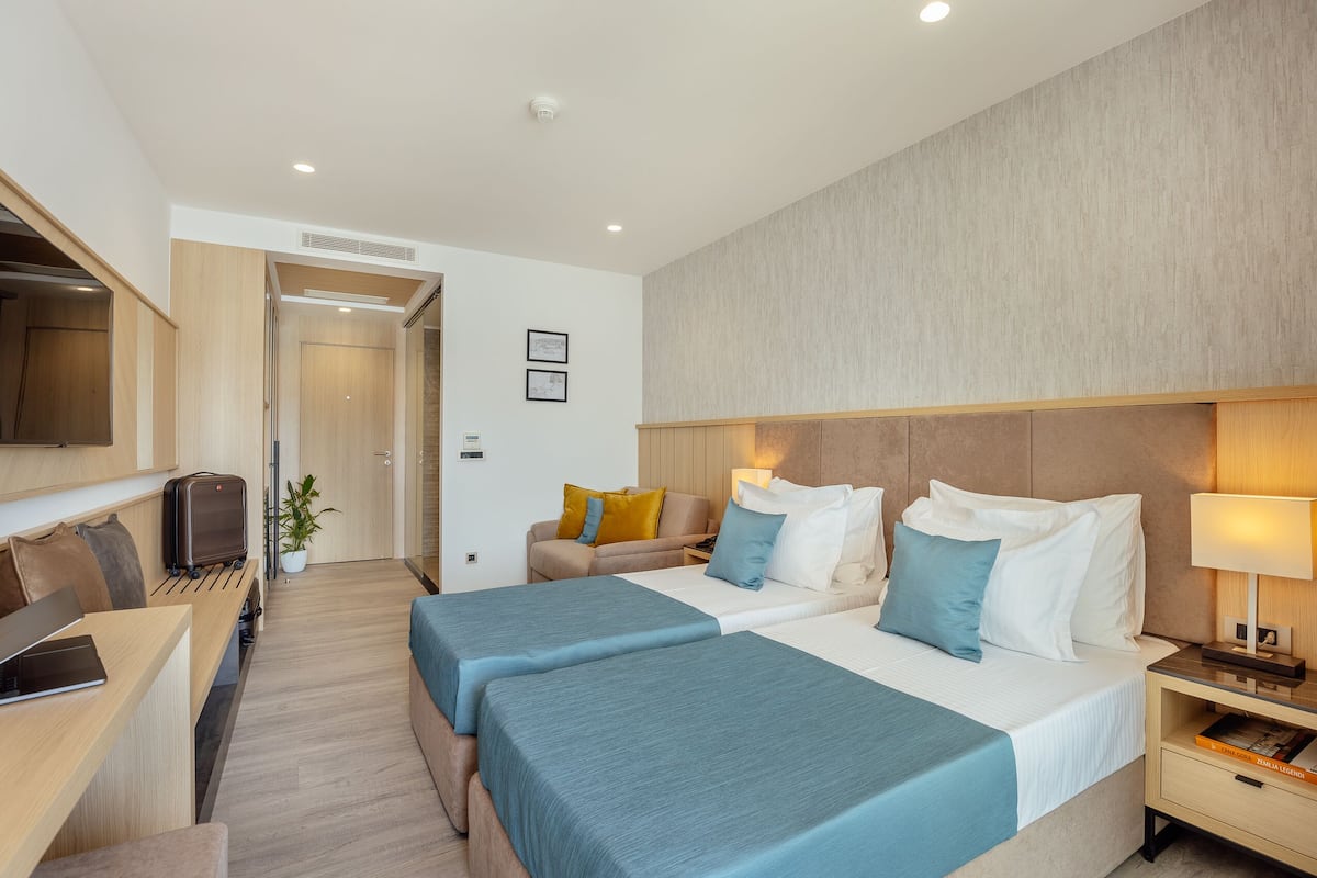 A hotel room with two beds, a desk, a TV, and a sofa.